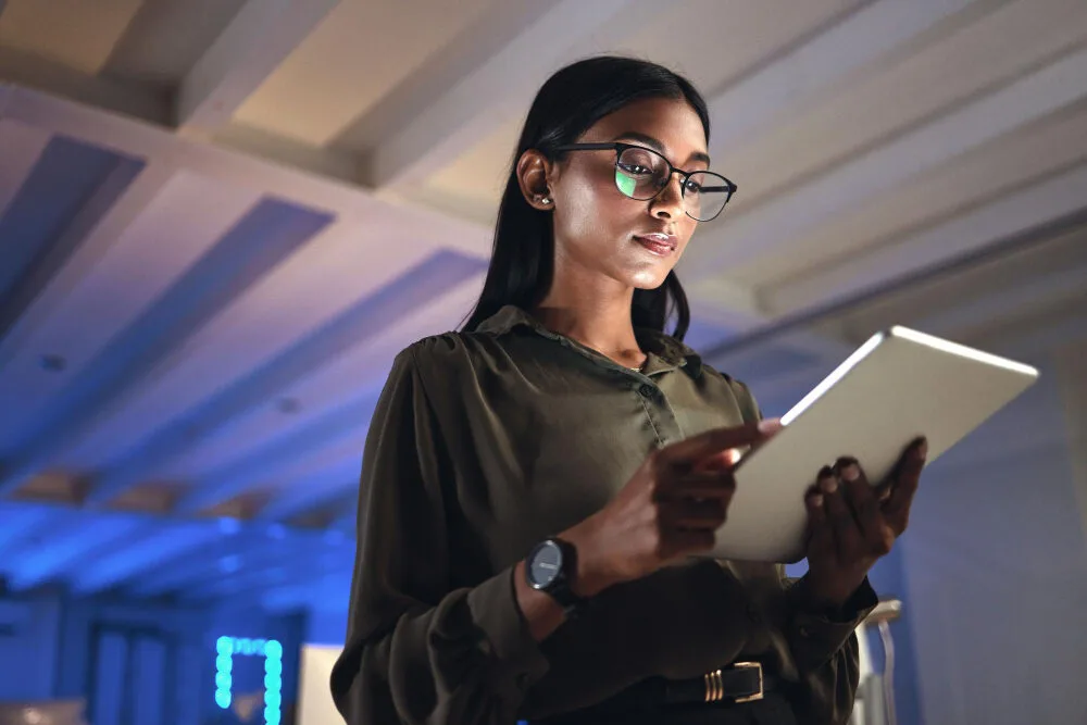 Femme à lunettes lisant sur une tablette dans un espace de travail moderne