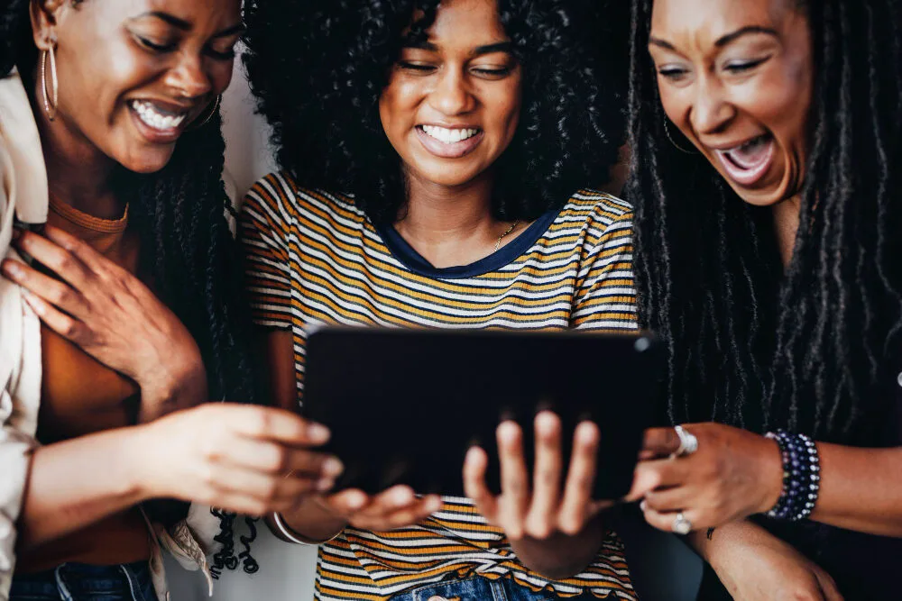Trois jeunes femmes souriantes regardent ensemble une tablette