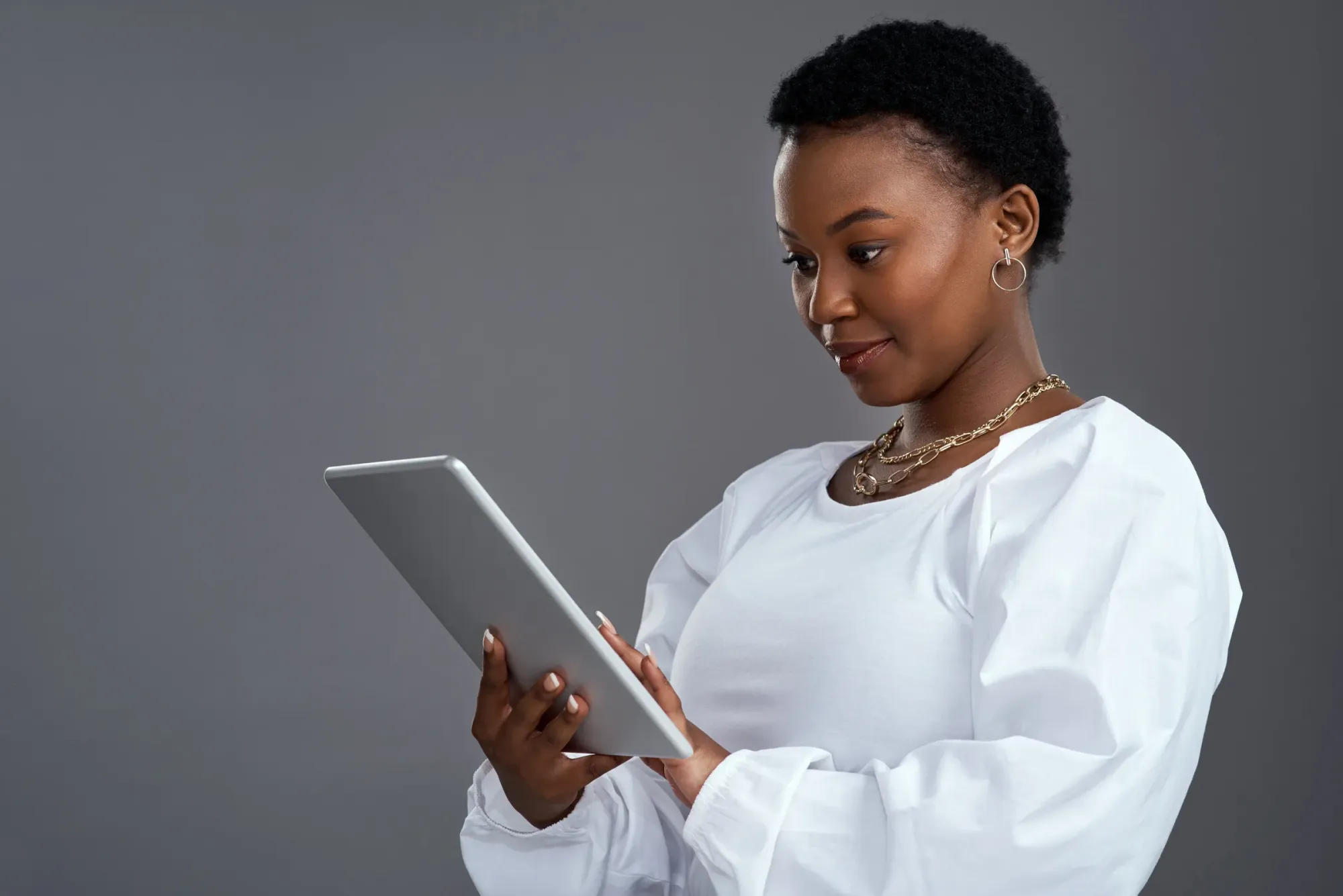Une femme en chemisier blanc, concentrée, consulte une tablette