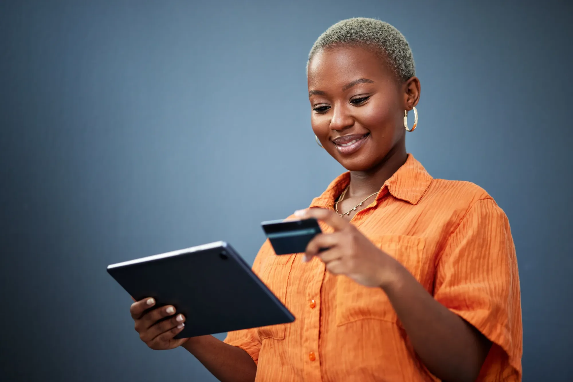Une femme souriante règle un achat en ligne, sa carte à la main, sur une tablette
