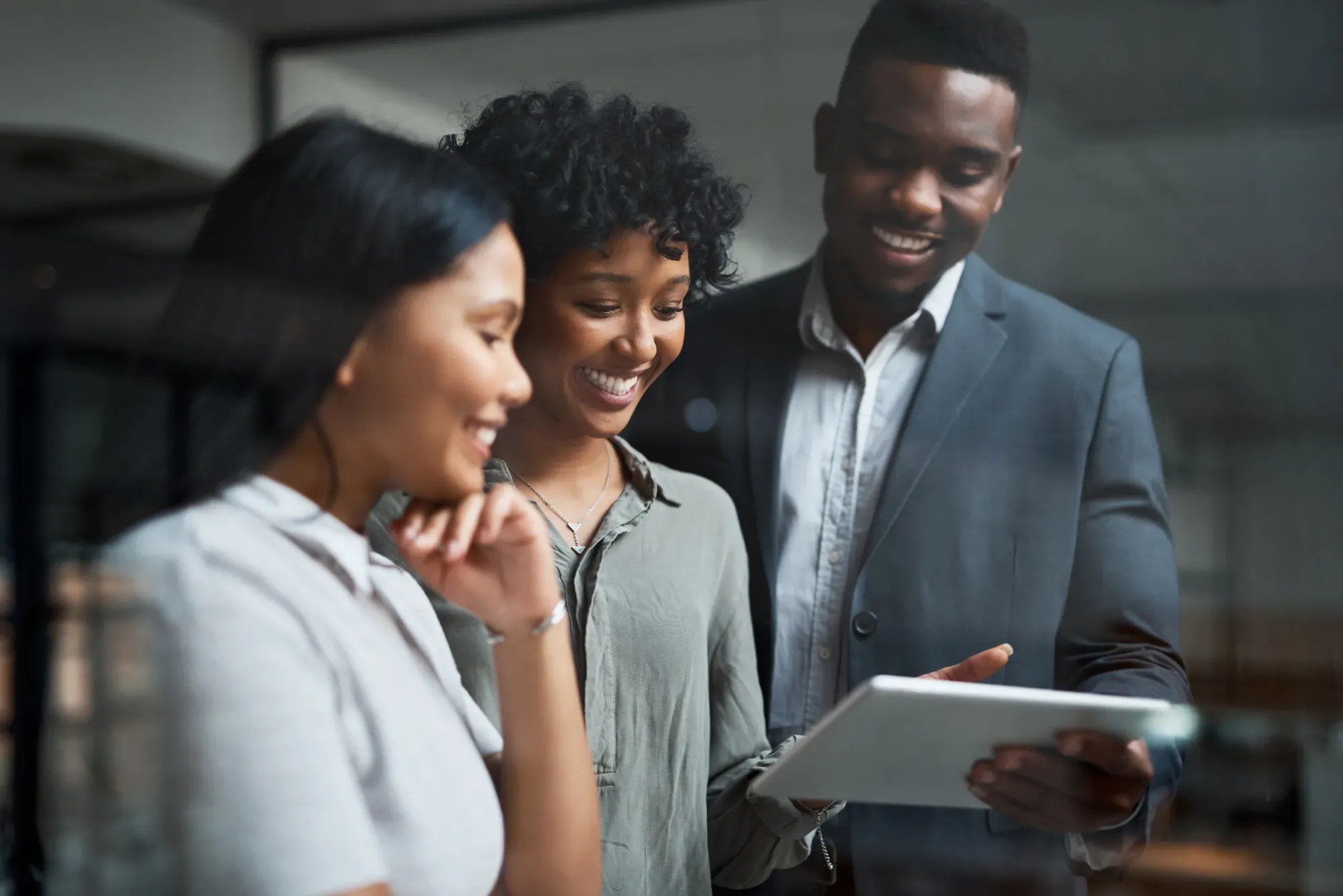 Trois collègues souriants regardent ensemble une tablette dans un bureau